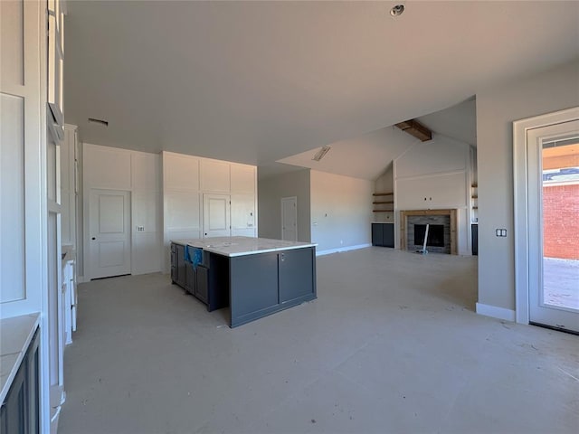 kitchen with a kitchen island, a fireplace, baseboards, white cabinetry, and vaulted ceiling