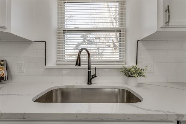 details featuring white cabinets, a sink, light stone countertops, and decorative backsplash