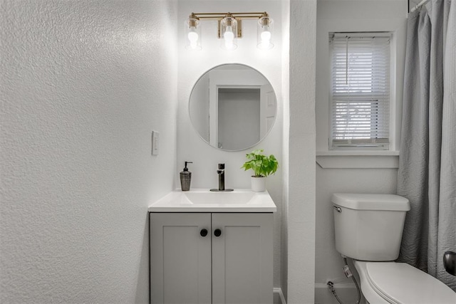 bathroom with a textured wall, toilet, and vanity