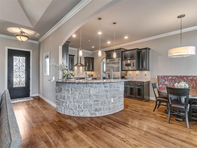 1109 Salvo Bridge Ct, Edmond, OK 73034 - kitchen with built in appliances, light stone counters, wall chimney range hood, arched walkways, and tasteful backsplash