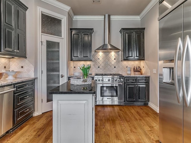 1109 Salvo Bridge Ct, Edmond, OK 73034 - kitchen with appliances with stainless steel finishes, wall chimney range hood, light wood-style flooring, crown molding, and tasteful backsplash