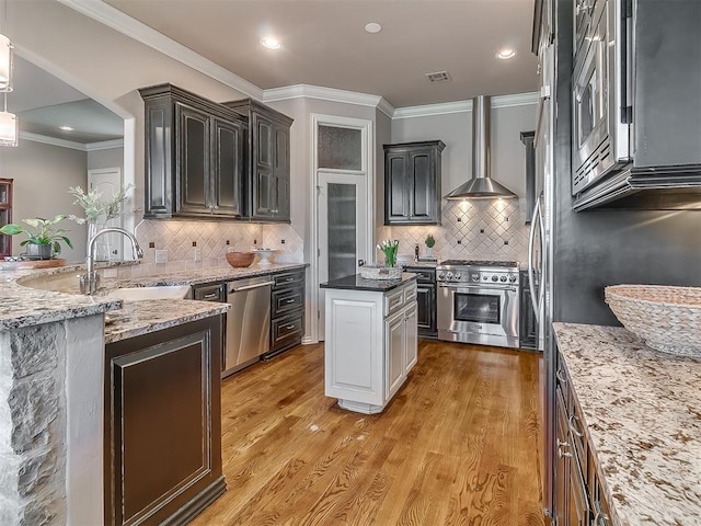 1109 Salvo Bridge Ct, Edmond, OK 73034 - kitchen featuring appliances with stainless steel finishes, wall chimney range hood, light wood-style floors, light stone countertops, and crown molding