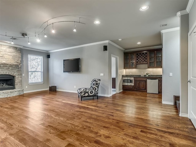 1109 Salvo Bridge Ct, Edmond, OK 73034 - unfurnished living room featuring crown molding, wet bar, dark wood finished floors, a stone fireplace, and recessed lighting