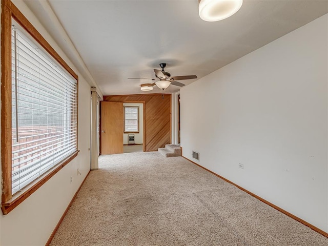 carpeted spare room featuring baseboards, visible vents, wood walls, and a ceiling fan