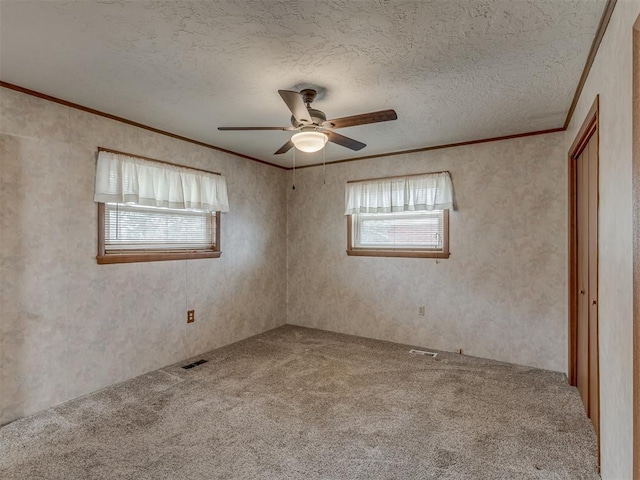 carpeted spare room with a textured ceiling, visible vents, and crown molding