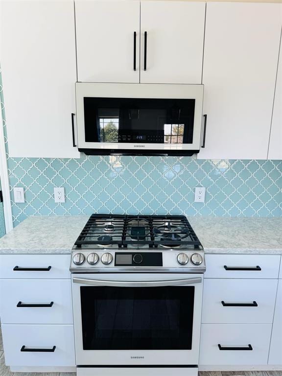 9514 N Woodchuck Ct, Edmond, OK 73034 - kitchen with stainless steel range with gas stovetop, backsplash, light stone counters, white cabinets, and white microwave