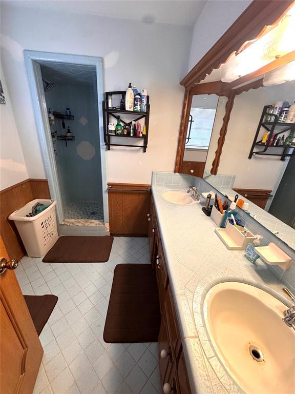 full bath with a sink, a stall shower, and wainscoting
