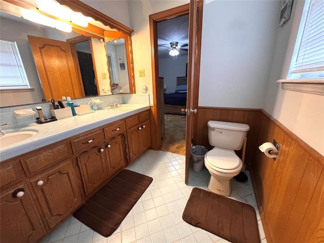 bathroom featuring ceiling fan, a sink, toilet, and wainscoting