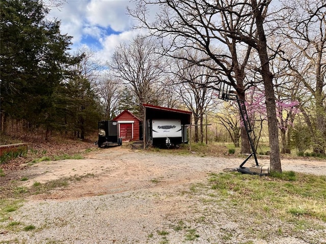 view of yard with a carport, an outdoor structure, and dirt driveway