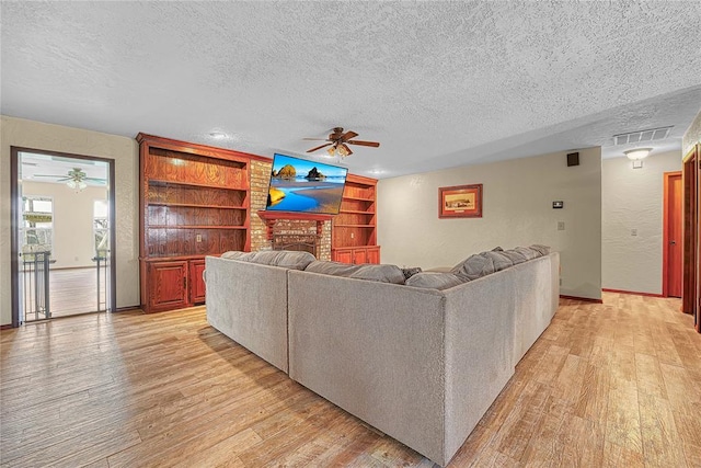 13989 US Highway 183, Hobart, OK 73651 - living room with a ceiling fan, a textured ceiling, light wood-style floors, built in shelves, and a fireplace