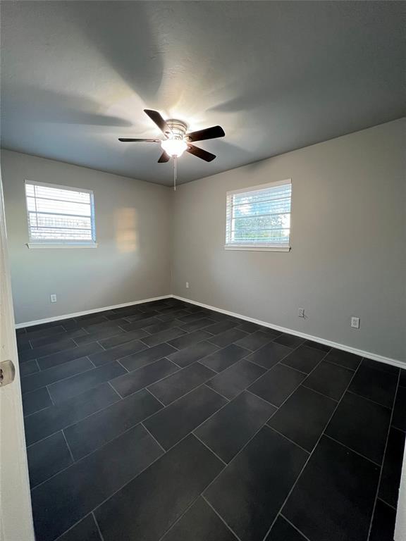 7440 NW 5th Ter, Oklahoma City, OK 73127 - unfurnished room featuring dark tile patterned floors, baseboards, a ceiling fan, and a healthy amount of sunlight