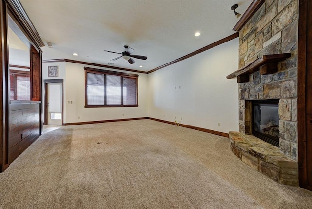 unfurnished living room with carpet floors, a stone fireplace, baseboards, ceiling fan, and ornamental molding