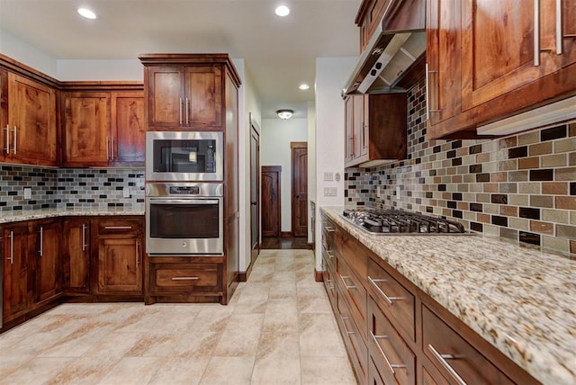 kitchen with stainless steel appliances, light stone countertops, tasteful backsplash, and extractor fan