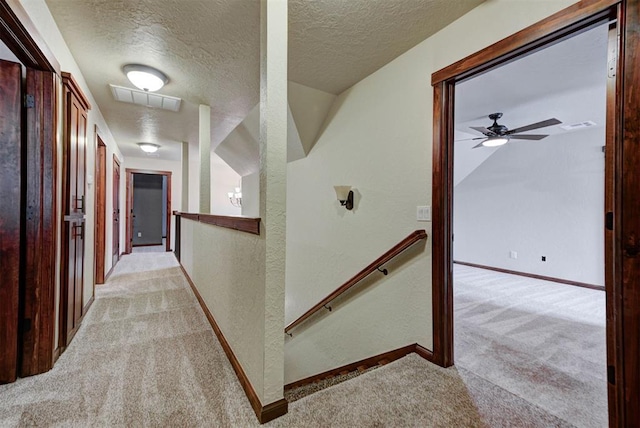 hallway featuring a textured wall, a textured ceiling, light colored carpet, and visible vents