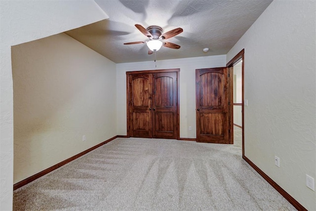 unfurnished bedroom featuring a textured ceiling, carpet, baseboards, a ceiling fan, and a textured wall