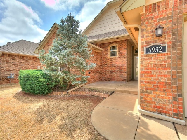 view of exterior entry featuring brick siding and roof with shingles
