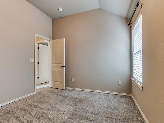 empty room featuring carpet flooring, baseboards, and lofted ceiling