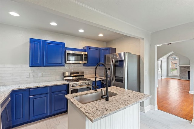 923 NE 19th St, Oklahoma City, OK 73105 - kitchen with stainless steel appliances, a sink, arched walkways, tasteful backsplash, and blue cabinetry