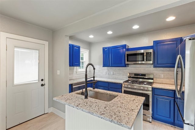 923 NE 19th St, Oklahoma City, OK 73105 - kitchen with stainless steel appliances, blue cabinetry, a sink, decorative backsplash, and light wood-type flooring
