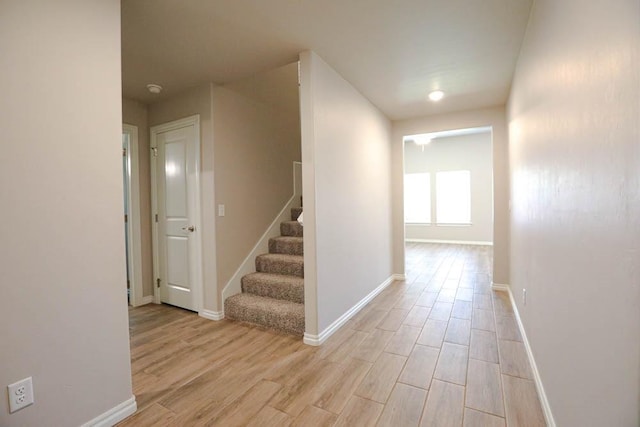 hall with light wood-style floors, stairway, and baseboards