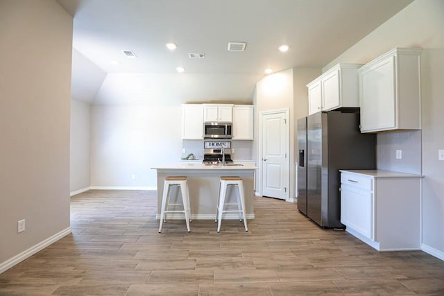 kitchen featuring an island with sink, light wood finished floors, white cabinets, appliances with stainless steel finishes, and visible vents