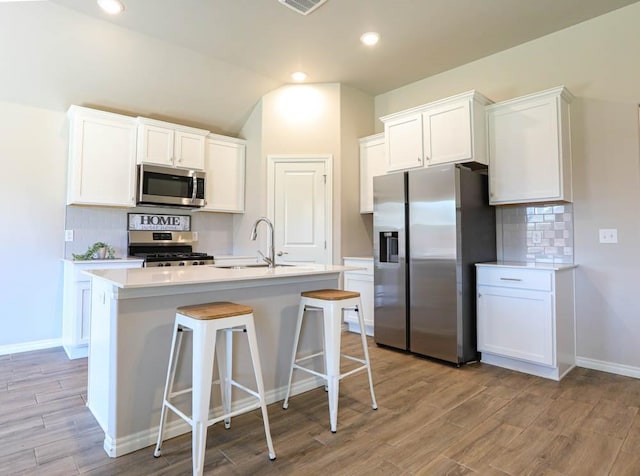 kitchen featuring decorative backsplash, stainless steel appliances, white cabinets, and a sink