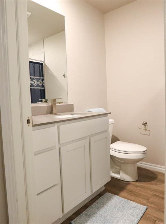 bathroom featuring baseboards, wood finished floors, vanity, and toilet