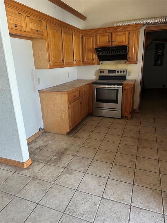 kitchen with light tile patterned flooring, brown cabinetry, stainless steel electric range, and extractor fan