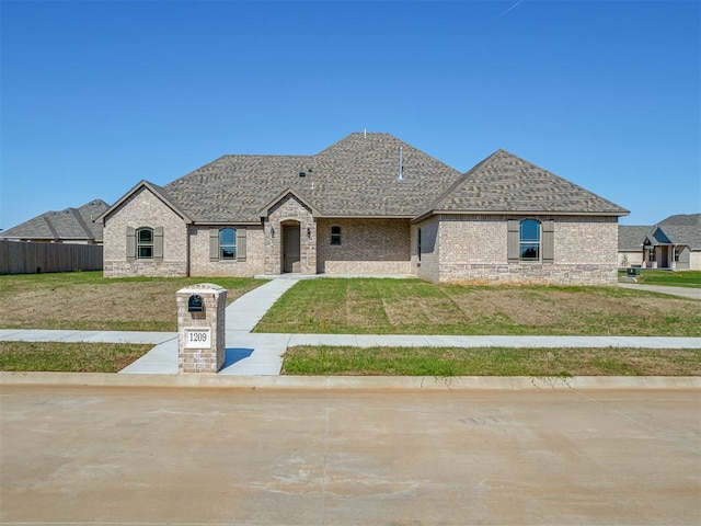 1209 Jozie Way, Tuttle, OK 73089 - french country style house with brick siding, fence, a shingled roof, and a front lawn