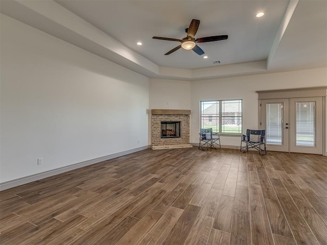 1209 Jozie Way, Tuttle, OK 73089 - unfurnished living room with dark wood-style flooring, a fireplace, ceiling fan, a tray ceiling, and french doors