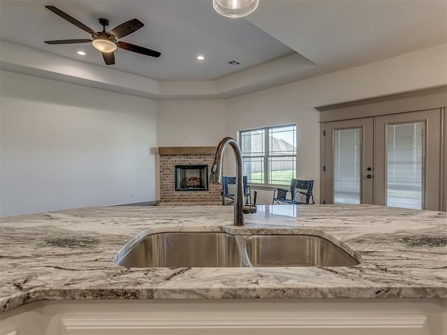 1209 Jozie Way, Tuttle, OK 73089 - kitchen with a brick fireplace, light stone counters, a raised ceiling, french doors, and a sink