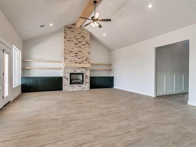 unfurnished living room featuring wood finished floors, a large fireplace, visible vents, beamed ceiling, and ceiling fan