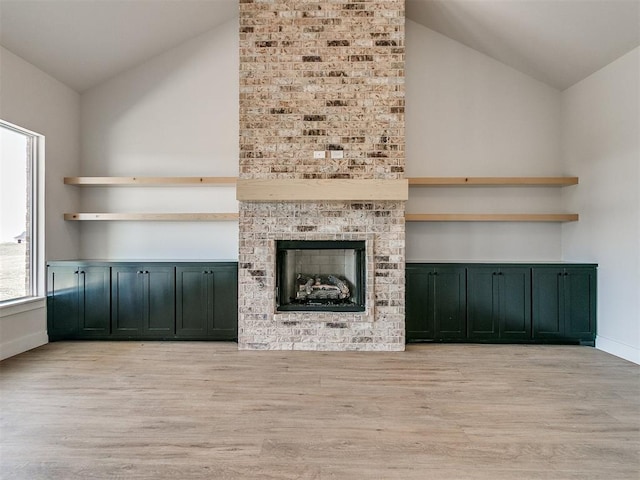 unfurnished living room with light wood-style flooring, a brick fireplace, baseboards, and vaulted ceiling