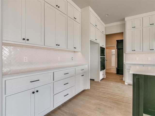 kitchen with light countertops, light wood-style flooring, white cabinets, stainless steel oven, and black microwave