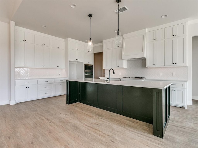 kitchen featuring white cabinets, visible vents, premium range hood, a sink, and a large island