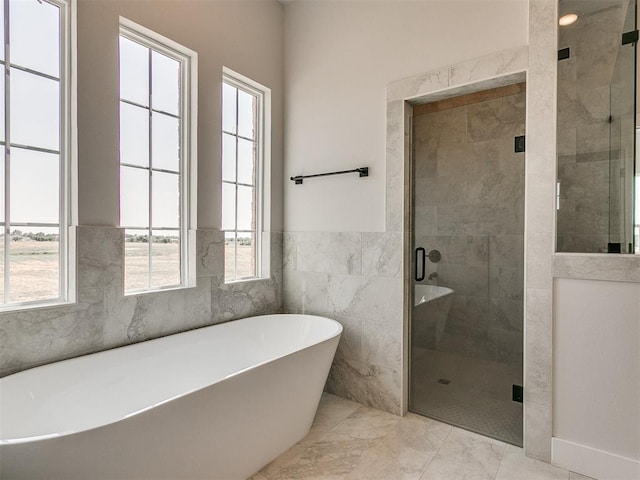 bathroom featuring marble finish floor, a stall shower, a soaking tub, and wainscoting