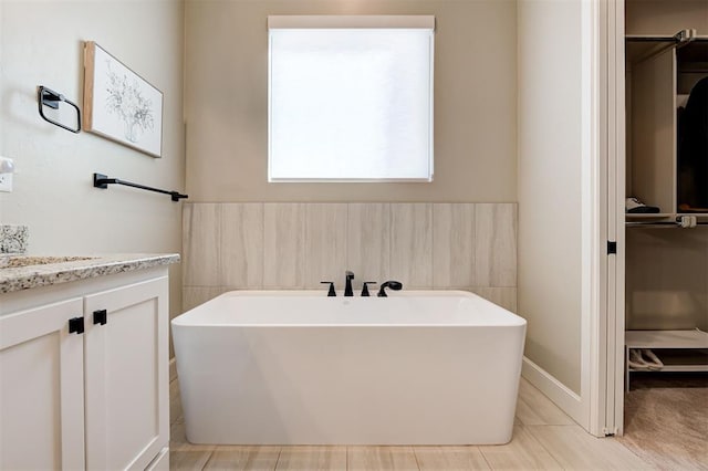 bathroom with a freestanding bath, a spacious closet, and vanity