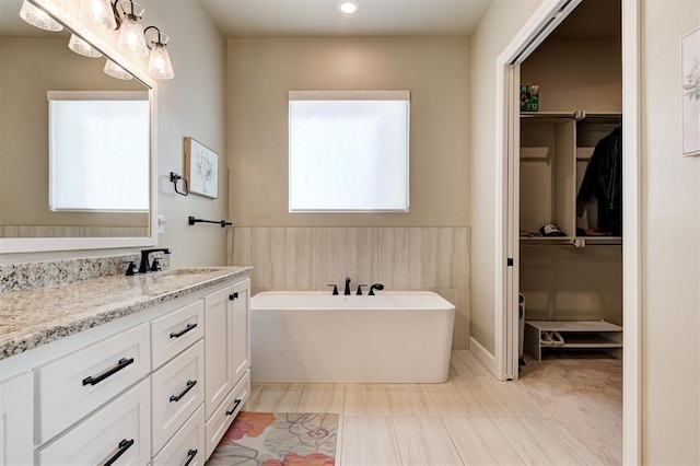full bath featuring a spacious closet, a freestanding tub, vanity, and tile patterned flooring