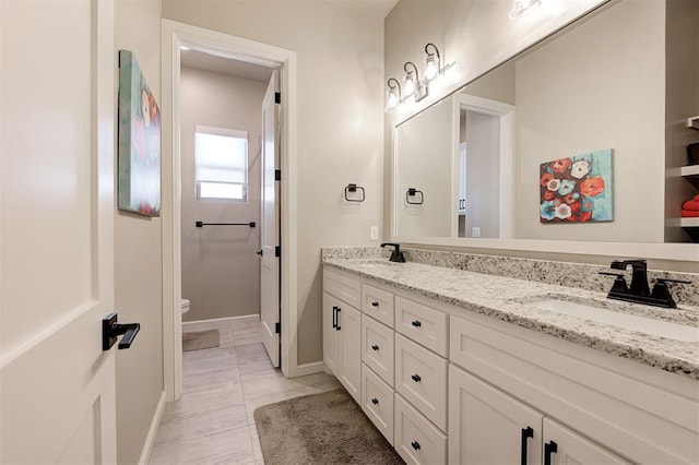 bathroom featuring double vanity, baseboards, a sink, and toilet
