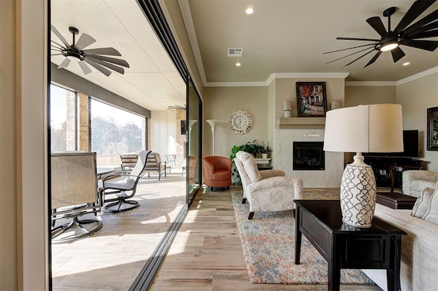 living area with a tiled fireplace, visible vents, a ceiling fan, and light wood-style flooring