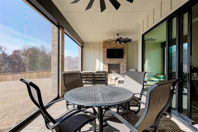 sunroom / solarium featuring outdoor dining space, an outdoor brick fireplace, a ceiling fan, and wood finished floors