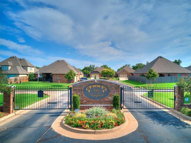 community sign featuring a residential view, a gate, fence, and a yard
