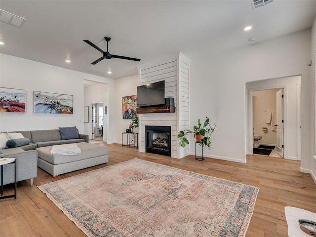 living area with a fireplace, visible vents, light wood-style floors, and ceiling fan