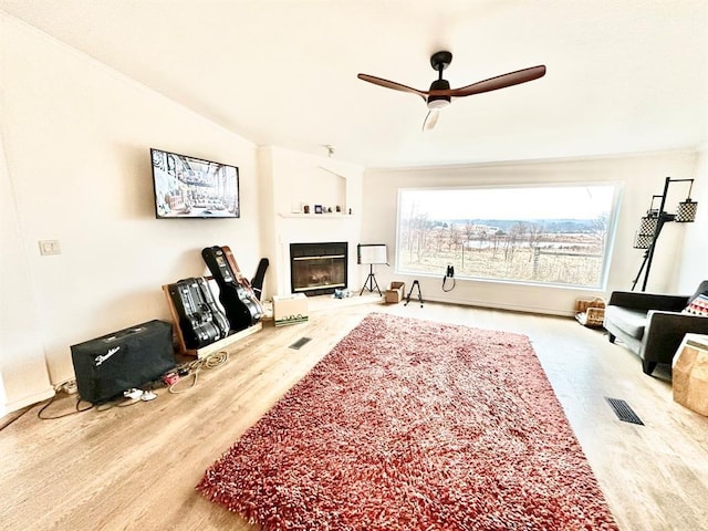 living area featuring crown molding, visible vents, a ceiling fan, a glass covered fireplace, and wood finished floors