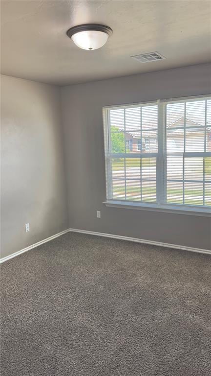 empty room with dark colored carpet, visible vents, and baseboards