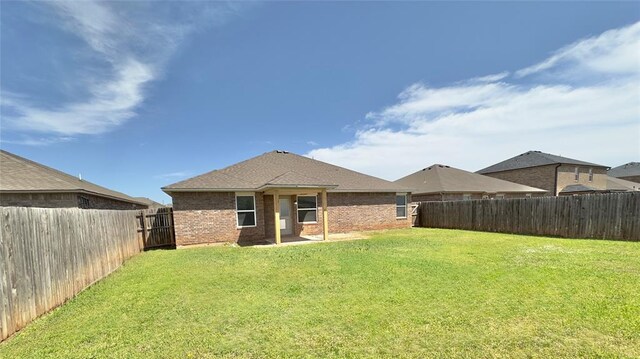 back of house featuring a lawn, a fenced backyard, and brick siding