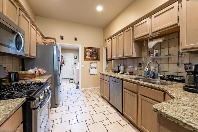 kitchen with backsplash, light stone countertops, a sink, and appliances with stainless steel finishes