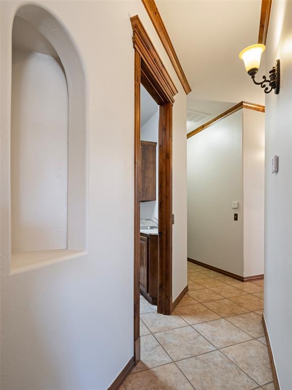 corridor featuring arched walkways, baseboards, and light tile patterned flooring