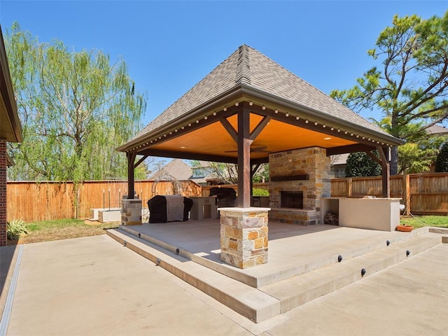 view of patio / terrace with a gazebo, a fenced backyard, and an outdoor stone fireplace