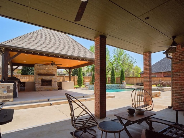 view of patio with a gazebo, a fenced backyard, ceiling fan, and an outdoor stone fireplace